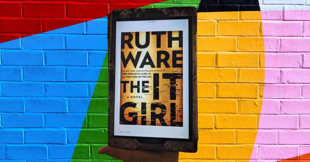 An eReader displaying the cover of The It Girl along a backdrop of painted bricks