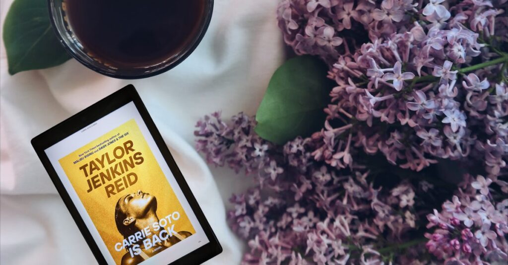 eReader displaying cover of Carrie Soto is Back with a purple flower and a cup of coffee/tea in the background