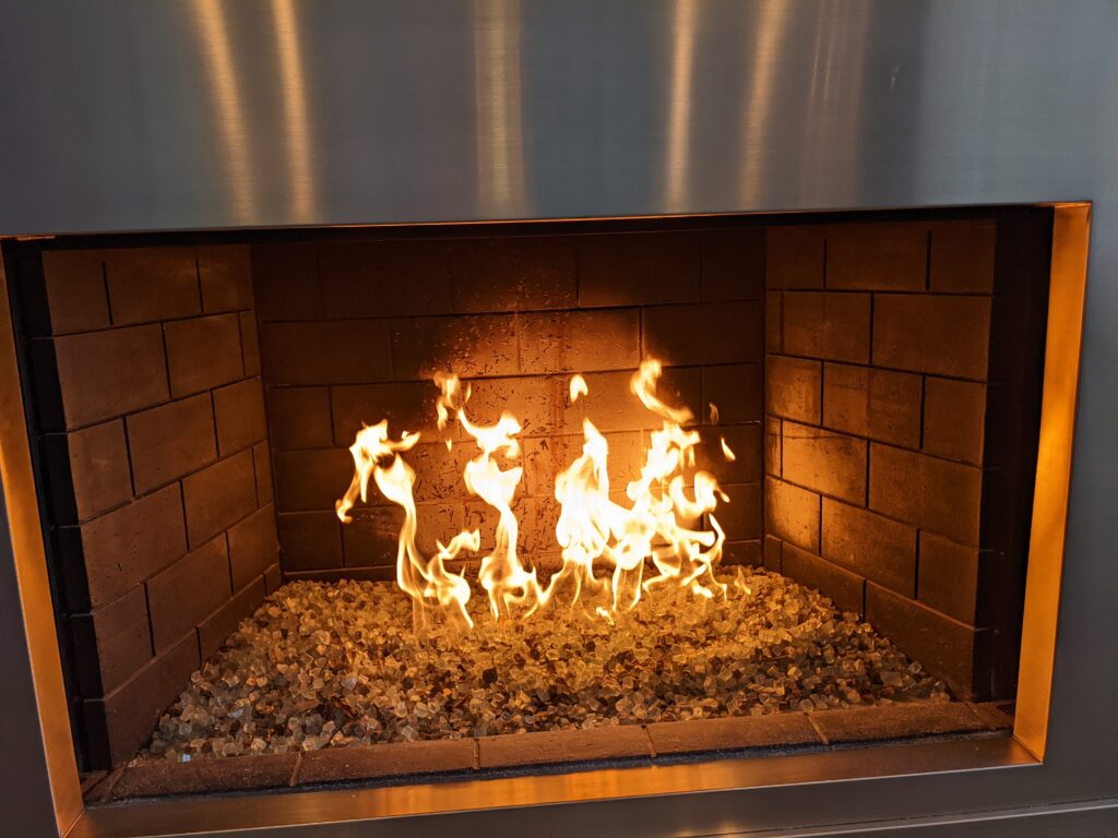 A lit gas fireplace with silver trim and white stones